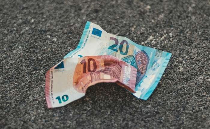 Zerknitterte 10- und 20-Euro-Banknoten liegen auf einem rauen Asphaltboden.