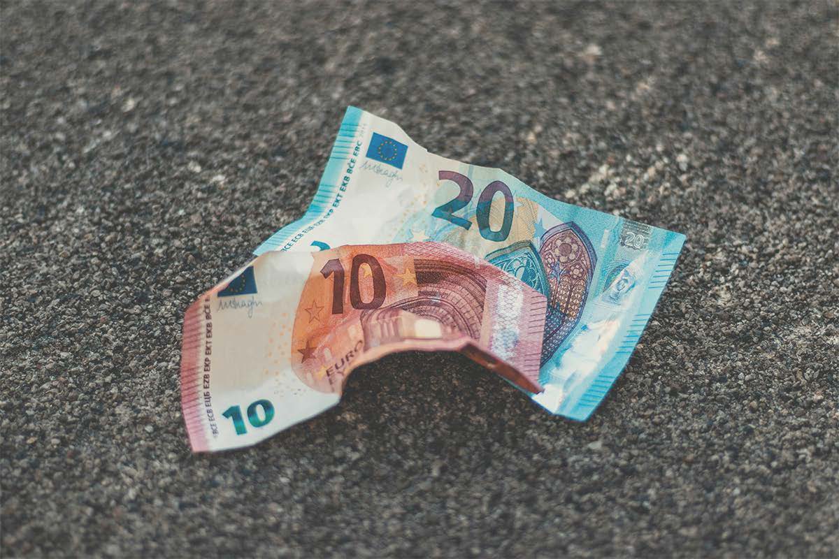 Zerknitterte 10- und 20-Euro-Banknoten liegen auf einem rauen Asphaltboden.