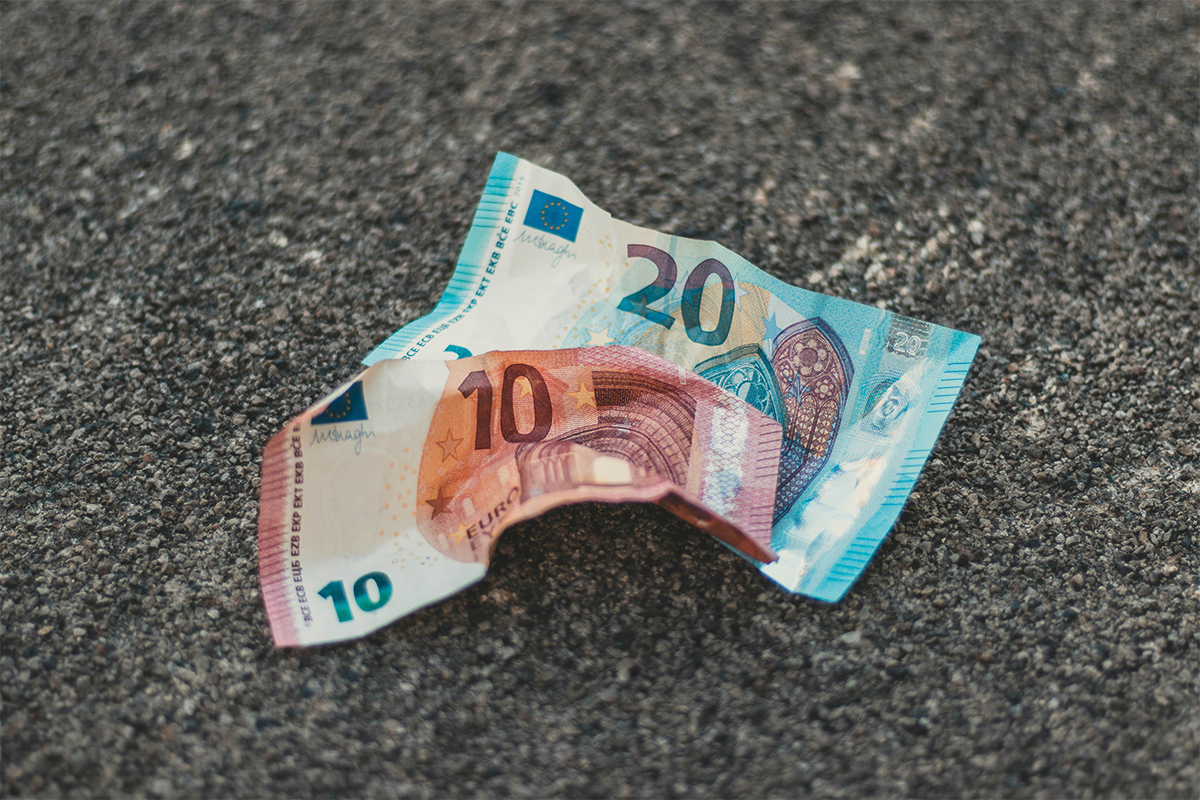 Zerknitterte 10- und 20-Euro-Banknoten liegen auf einem rauen Asphaltboden.