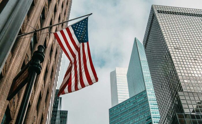 US-Flagge vor modernen Hochhäusern in einer amerikanischen Innenstadt.
